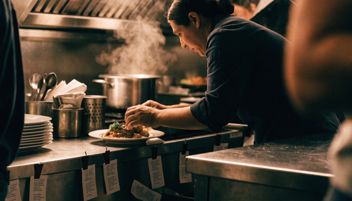 A cook plating a dish at the pass
